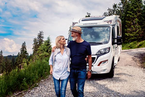 Fahrzeug mieten, einsteigen, Urlaub genießen 2 Paar steht lächelnd vor einem Wohnwagen in schöner Landschaft