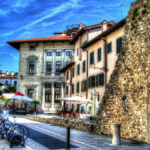 a stone wall with a stone wall and a building with a bike rack in Udine