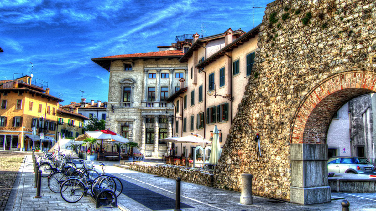 Neues Radlerparadies: Udine und Umland 1 a stone wall with a stone wall and a building with a bike rack in Udine