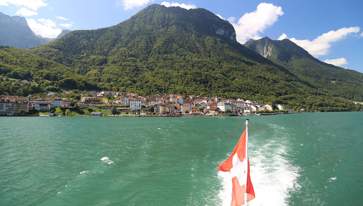 Sonnige Schweizer Riviera: Magnet für Stars 3 Das Foto ist von einem Schiff mit Blick auf die Schweizer Riviera aufgenommen. Man sieht die Schweizer Flagge, den See und Berge im Hintergrund