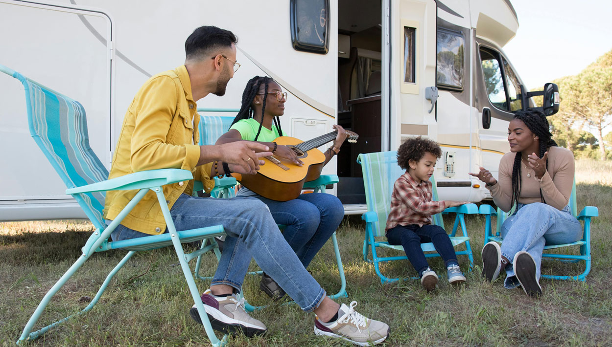 11 Gründe, warum Camping süchtig macht 5 Eine Familie sitzt vorf dem Wohnmobil im Freien