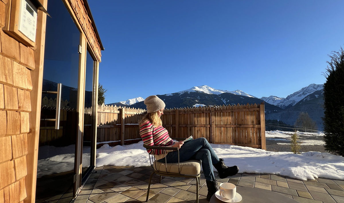 JOMO-Urlaub: Die Kunst des Nichtstuns 18 Frau sitzt lesend auf der Terrasse in der Wintersonne