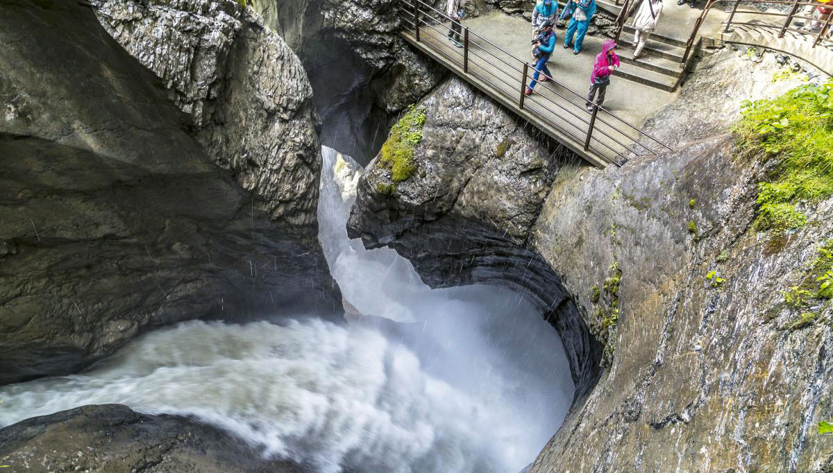 Top 10 Fotostopps in den Westalpen 4 Menschen schauen auf das mposante Wasser an einem der Trümmelbachfälle