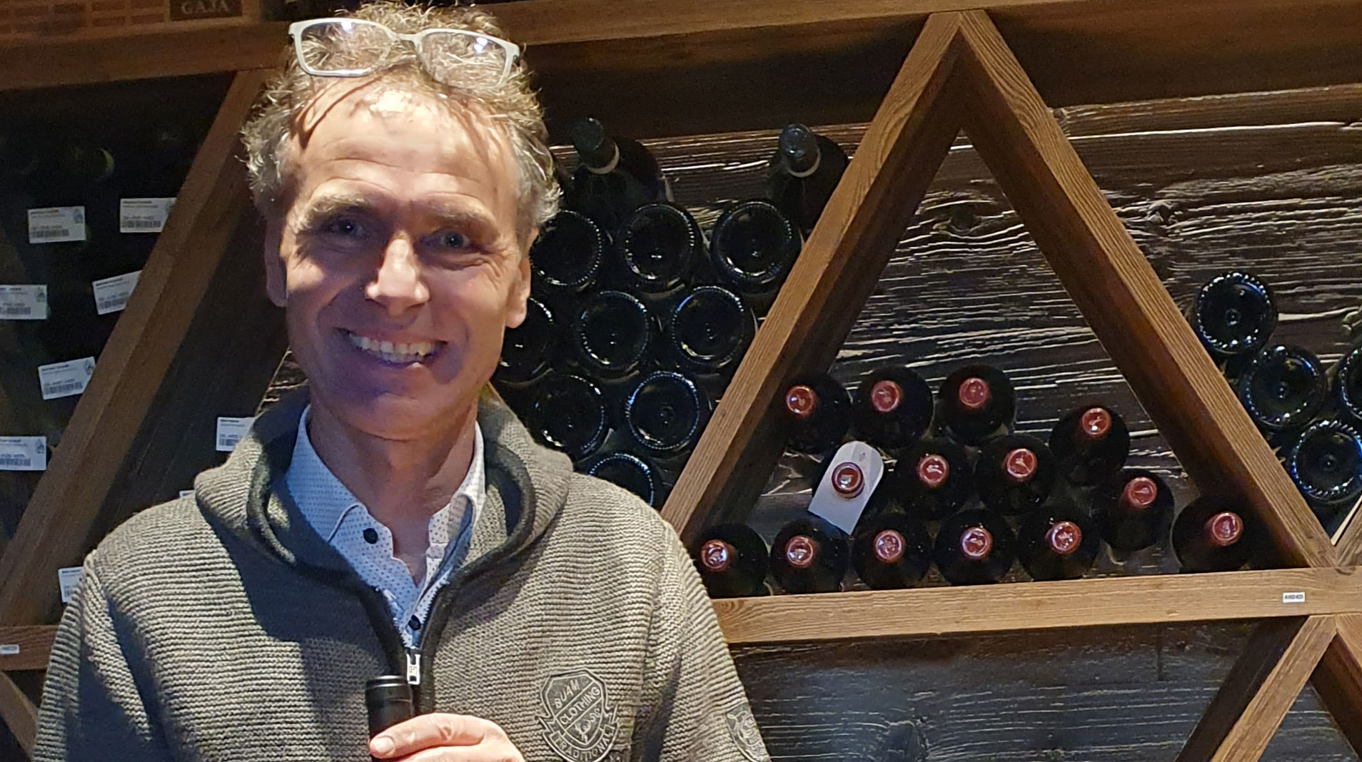 Markus Valentini steht vor einem Flaschenregal voller Weine und ist Vordenker der Ladiner-Identität 