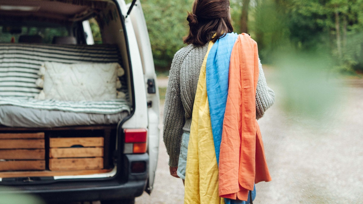 3 Outdoor-Textilien für den Alpenausflug 5 Person hat drei Handtücher auf dem Rücken und steht vor der geöffneten Heckklappe seines Campervans
