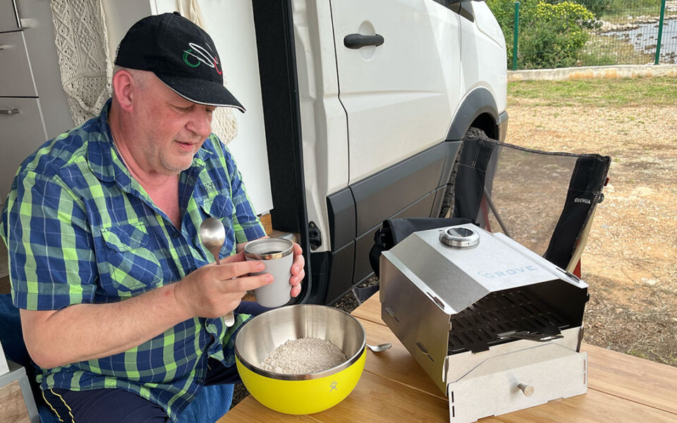 Ein Mann kocht mit Koch-Tools vor einem Campervan draußen