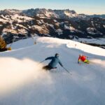 Für den frühen Wurm: Frühlingsurlaub in den Alpen 2026 7 Zwei Menschen sausen mit Skier die Piste in den Alpen im Wilden Kaiser herunter, und sind voller Vorfreude auf den nächsten Frühlingsurlaub