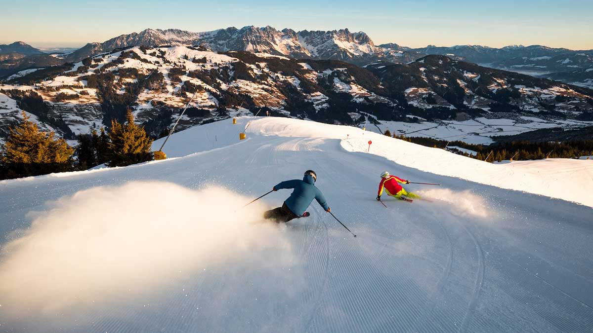 Für den frühen Wurm: Frühlingsurlaub in den Alpen 2026 1 Zwei Menschen sausen mit Skier die Piste in den Alpen im Wilden Kaiser herunter, und sind voller Vorfreude auf den nächsten Frühlingsurlaub